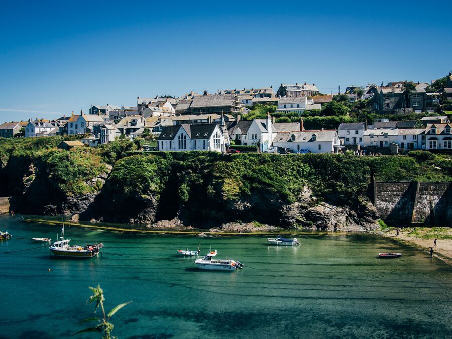 port isaac bay with boats on the crystal clear water and houses surrounding on the cliff tops
