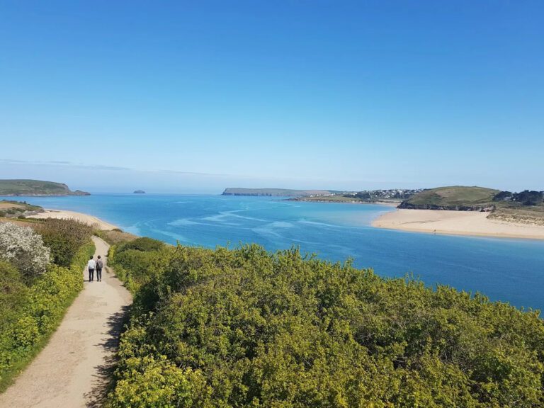 Looking over Padstow from the coastal walk. People walk ahead on the path on a blue sky day